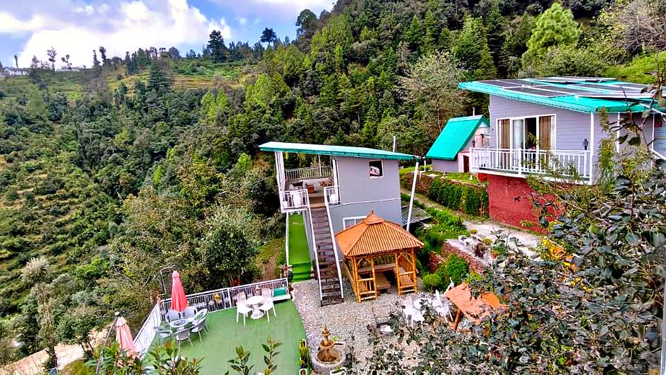 Cottages on a forested hillside with terraced valley views at The Rare One’s Resort, Mukteshwar