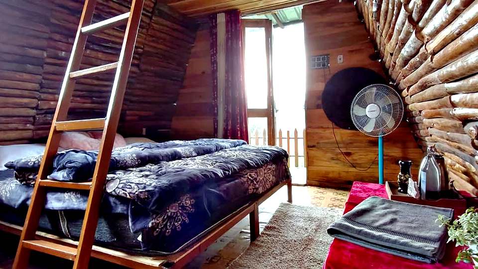 Double bed inside a log A-frame cottage at The Rare One’s Resort, Mukteshwar