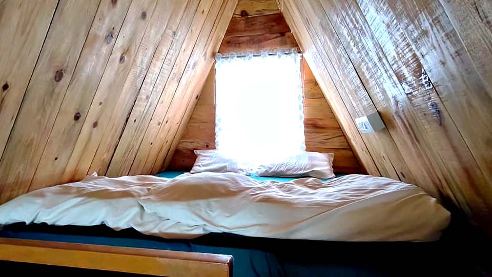 Pine-panelled A-frame cottage bedroom at The Rare One’s Resort, Mukteshwar