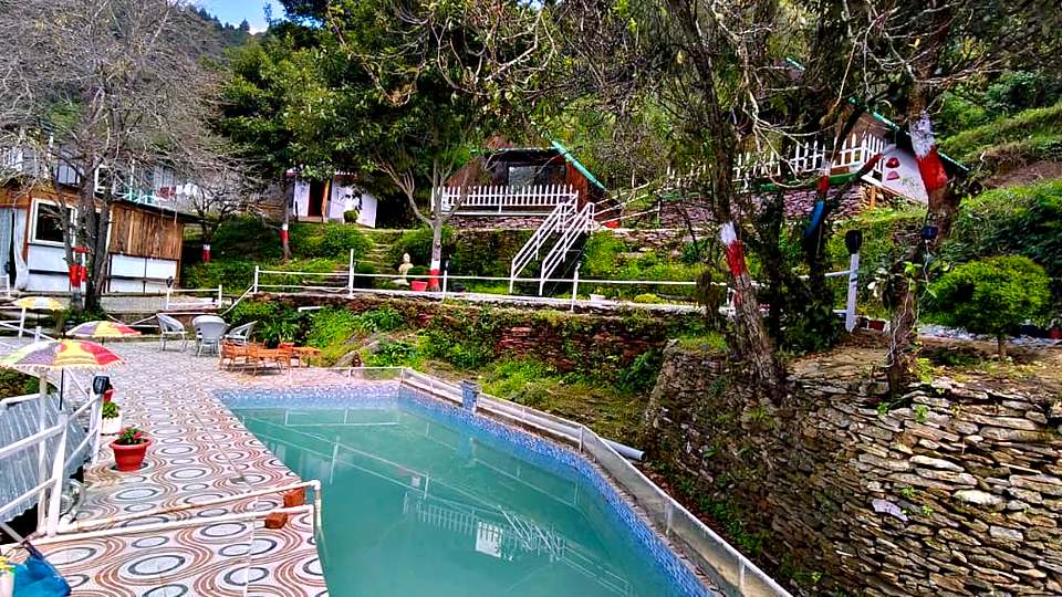 Swimming pool surrounded by trees and cottages at The Rare One’s Resort, Mukteshwar